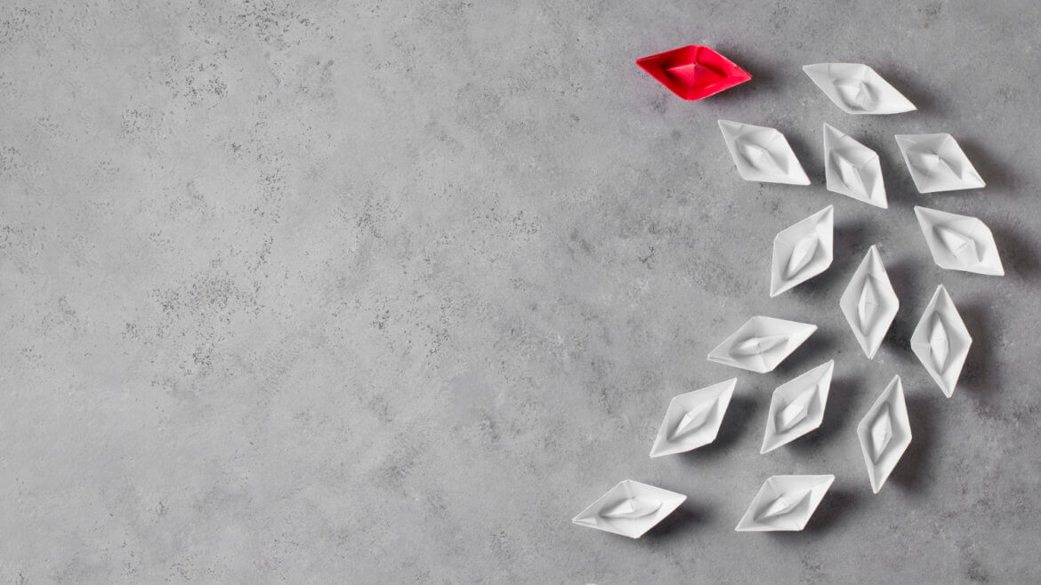 A group of white paper boats with a red paper boat leading them