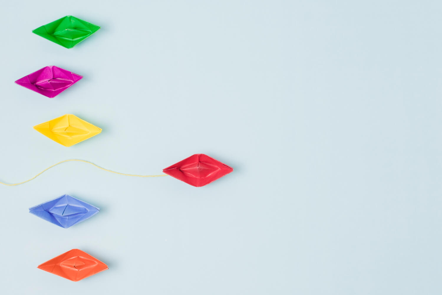A group of multicolored unique paper boats with a red boat ahead of the rest